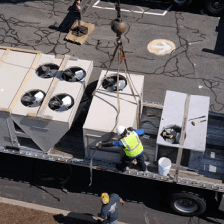 Construction workers lifting large units on a roof.