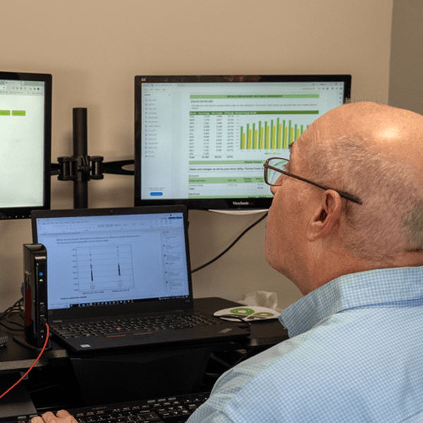 A man sitting at a desk and looking at three monitors.