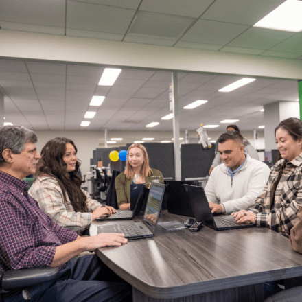 A group of people sitting around a table with laptops.