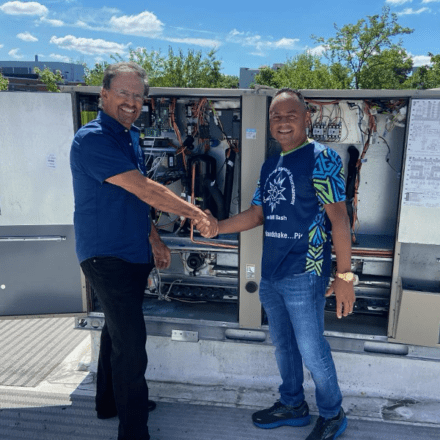 Two men shaking hands in front of an air conditioning unit.
