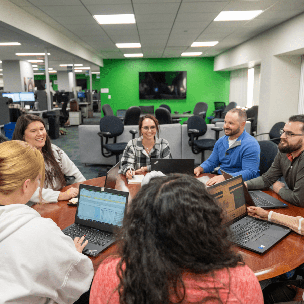 A group of people sitting around a table with laptops.