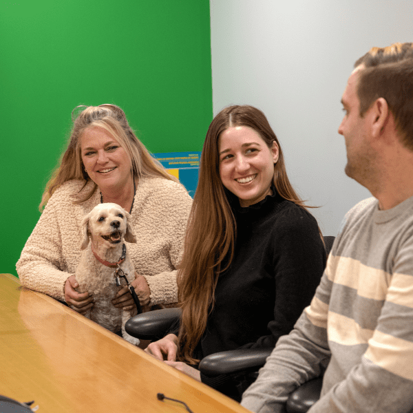 Group of people, one holding a dog, talking and smiling at a table.