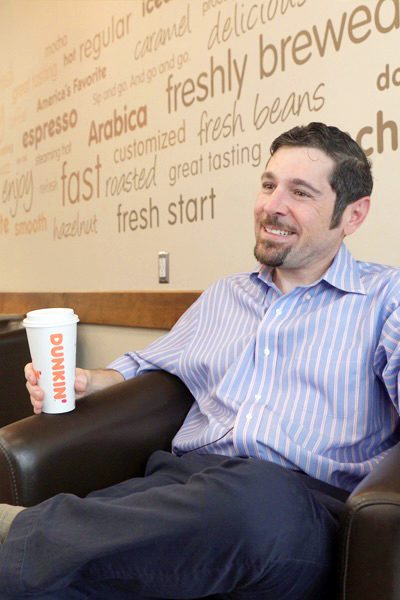 Man sitting at Dunkin' Donuts with a coffee in his hand.