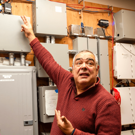 Man wearing a red sweater and pointing at units on a wall.