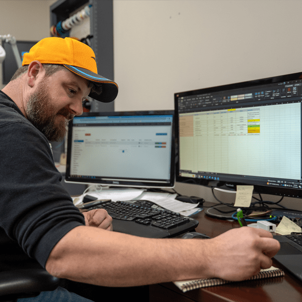 Man at his desk looking at monitors and writing down notes.